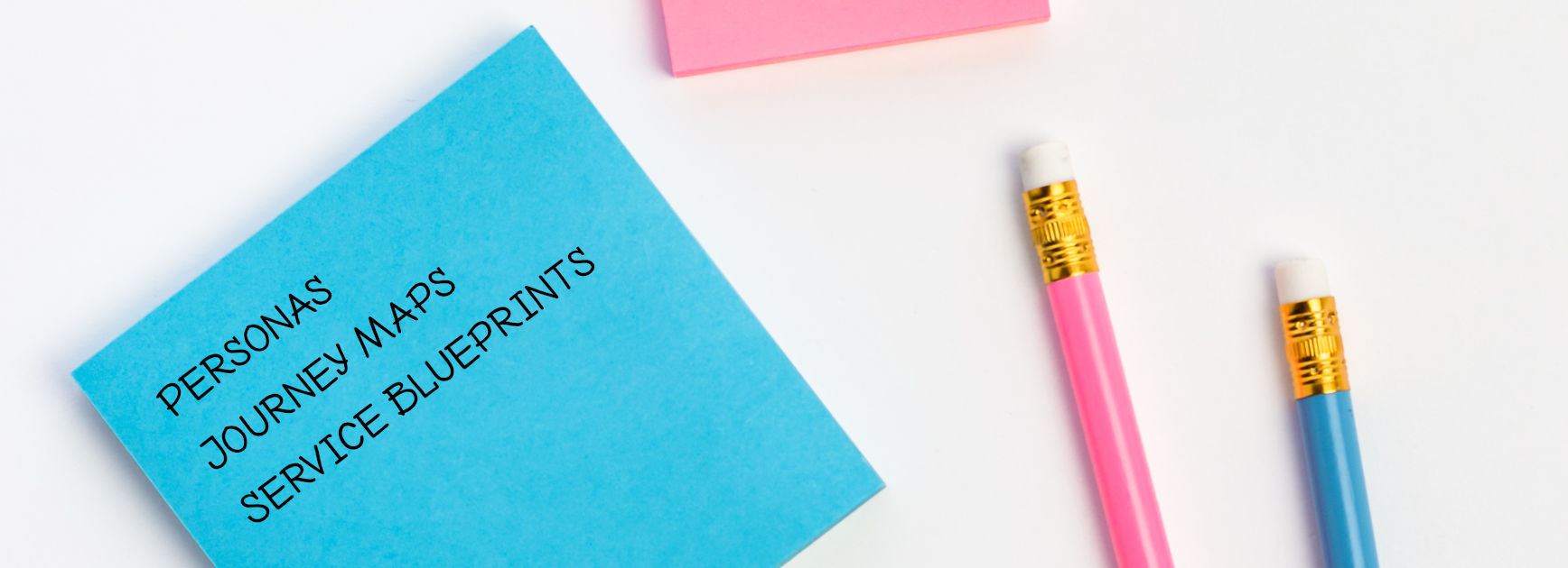 Image of sticky note pad listing personas, journey maps, and service blueprints next to two pencils